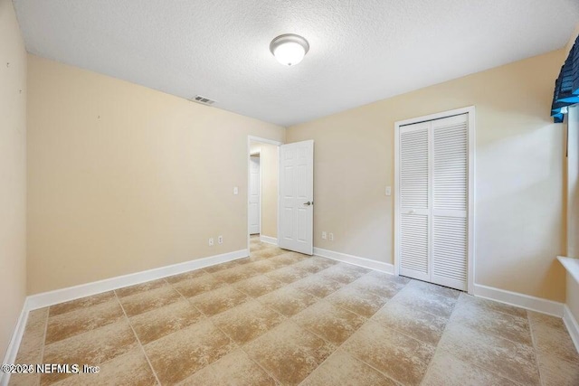 unfurnished bedroom with a closet, visible vents, a textured ceiling, and baseboards