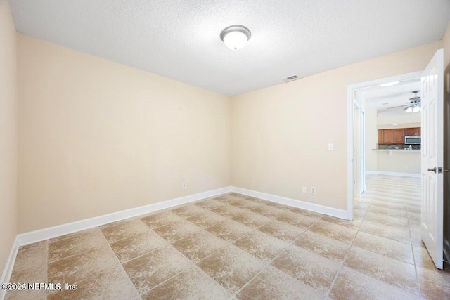 unfurnished room with a textured ceiling, baseboards, visible vents, and ceiling fan