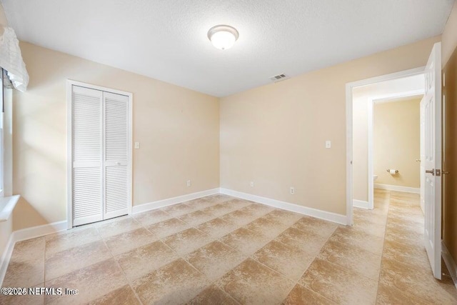 unfurnished bedroom featuring a closet, visible vents, a textured ceiling, and baseboards