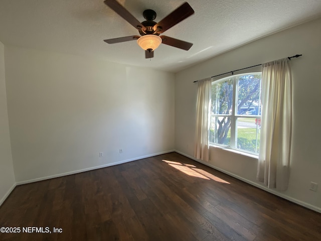 empty room featuring a textured ceiling, dark wood-type flooring, baseboards, and a ceiling fan