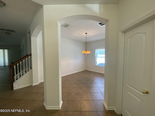 corridor featuring visible vents, dark tile patterned flooring, a textured ceiling, arched walkways, and stairs