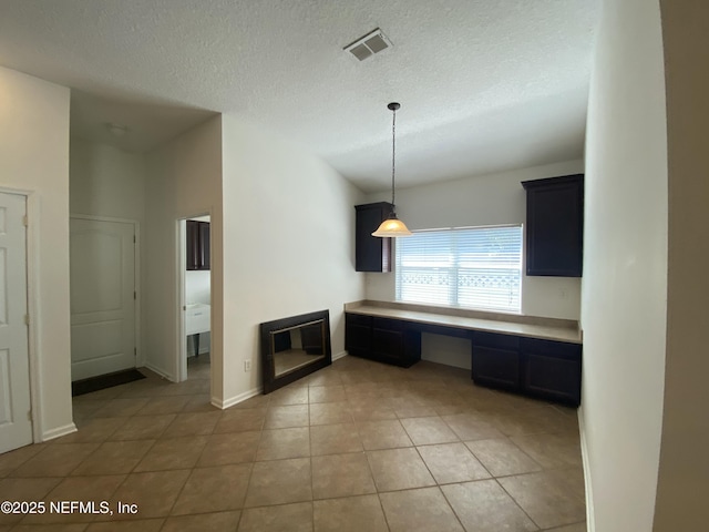 kitchen featuring visible vents, light tile patterned flooring, light countertops, built in desk, and a textured ceiling