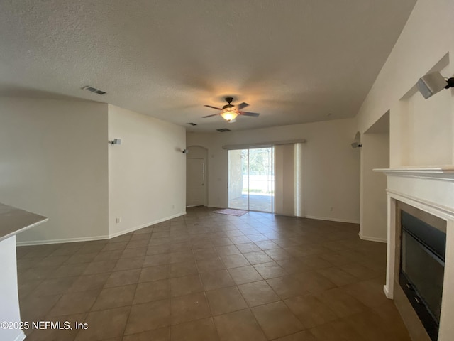 unfurnished living room featuring baseboards, a textured ceiling, a glass covered fireplace, and a ceiling fan