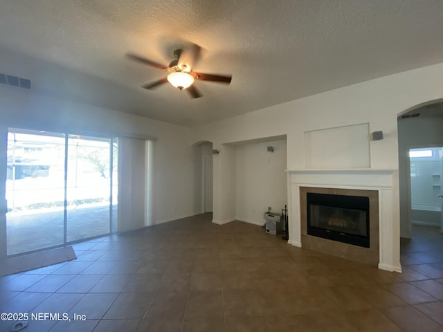 unfurnished living room featuring visible vents, a textured ceiling, arched walkways, a fireplace, and ceiling fan