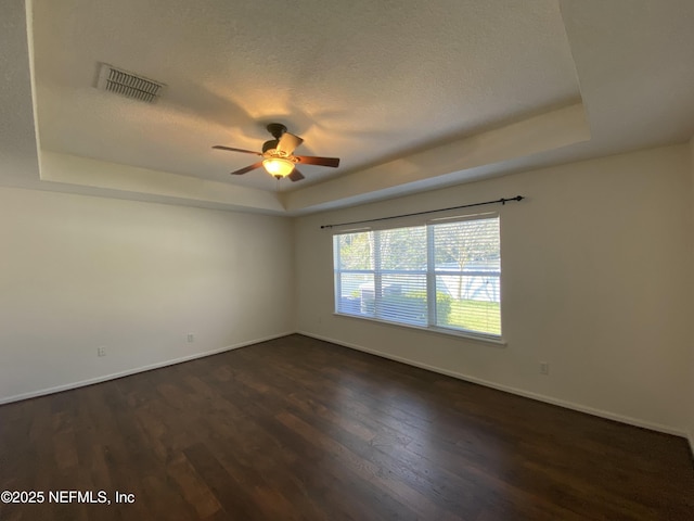 unfurnished room featuring a ceiling fan, visible vents, a tray ceiling, dark wood-type flooring, and a textured ceiling