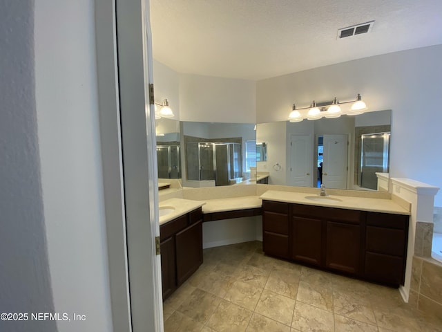 full bath featuring a sink, visible vents, two vanities, and a stall shower