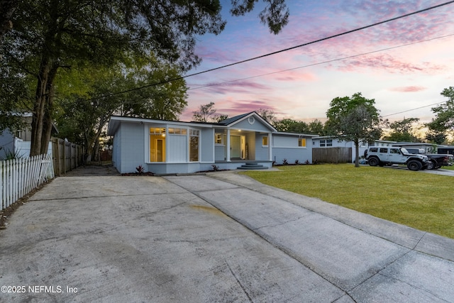 view of front of property with covered porch, concrete driveway, a yard, and fence