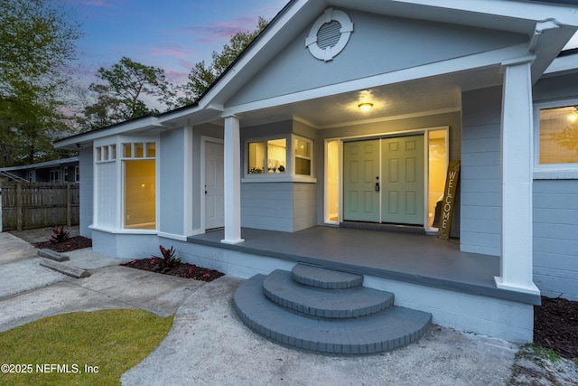 exterior entry at dusk featuring covered porch and fence