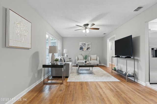 living area featuring wood finished floors, a ceiling fan, visible vents, baseboards, and a textured ceiling