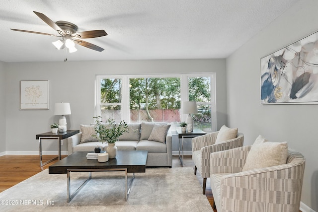 living area featuring a textured ceiling, baseboards, ceiling fan, and wood finished floors