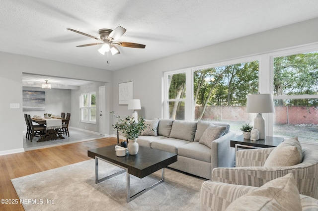 living area featuring baseboards, a textured ceiling, a ceiling fan, and wood finished floors