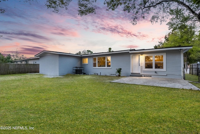 back of house at dusk featuring a patio area, a yard, and fence