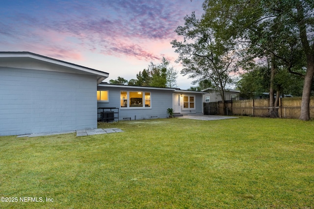 back of property at dusk with a patio area, fence, and a lawn