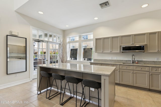 kitchen featuring a breakfast bar area, visible vents, gray cabinets, a sink, and stainless steel microwave