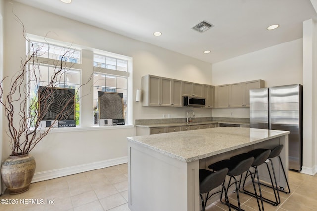 kitchen featuring visible vents, a kitchen island, light stone counters, gray cabinets, and stainless steel appliances