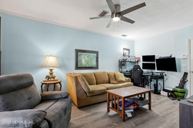 living area featuring visible vents, a ceiling fan, light wood-style floors, and ornamental molding