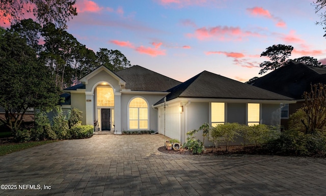 single story home featuring stucco siding, decorative driveway, an attached garage, and a shingled roof