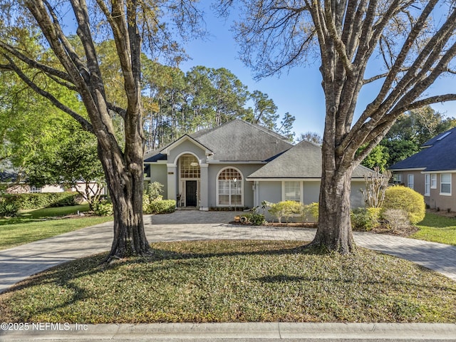 view of front of property featuring a shingled roof, a front lawn, decorative driveway, and stucco siding