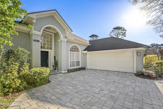 property entrance featuring stucco siding, a garage, roof with shingles, and driveway