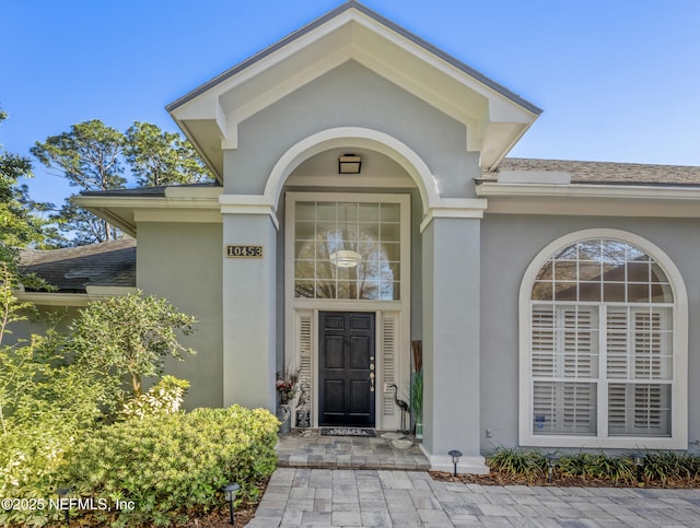 doorway to property with stucco siding and roof with shingles