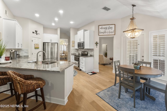 kitchen with light stone counters, light wood-style flooring, appliances with stainless steel finishes, a peninsula, and an inviting chandelier