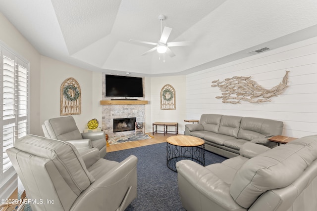 living room featuring visible vents, ceiling fan, a tray ceiling, a fireplace, and wood finished floors