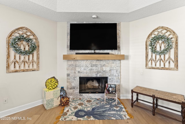 living area featuring baseboards, a textured ceiling, wood finished floors, and a fireplace