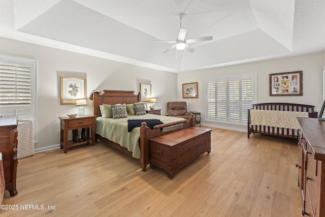 bedroom with a raised ceiling, light wood-style floors, and a textured ceiling