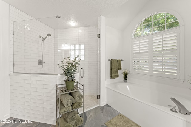 full bath with vaulted ceiling, a bath, a shower stall, and a textured ceiling