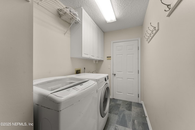 clothes washing area with cabinet space, washer and dryer, a textured ceiling, and baseboards