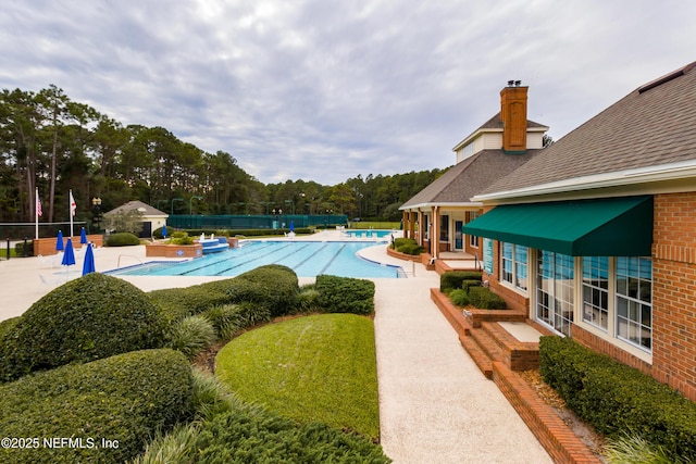 community pool featuring a patio, fence, and an outbuilding