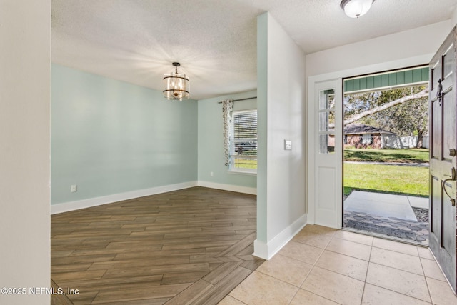 entrance foyer with a chandelier, a textured ceiling, baseboards, and wood finished floors