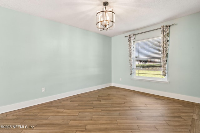 spare room featuring a notable chandelier, a textured ceiling, baseboards, and wood finished floors