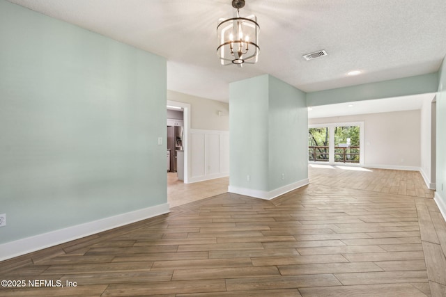 unfurnished room featuring wood finished floors, baseboards, visible vents, a textured ceiling, and a chandelier