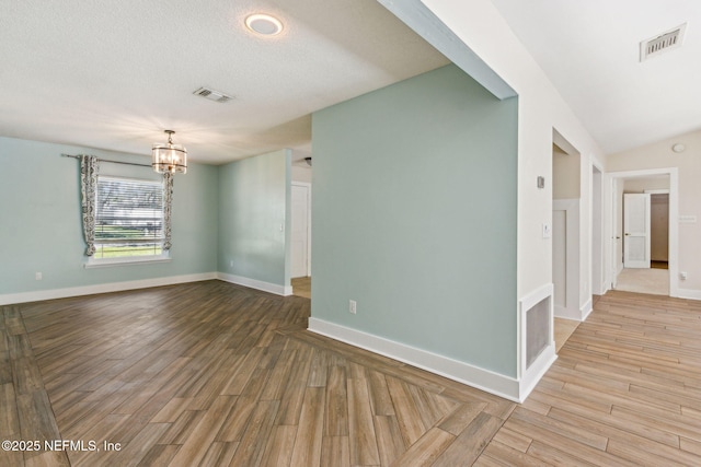 spare room with visible vents, an inviting chandelier, and wood finished floors