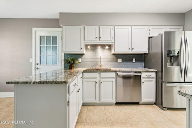 kitchen featuring appliances with stainless steel finishes, dark stone counters, a peninsula, and a sink