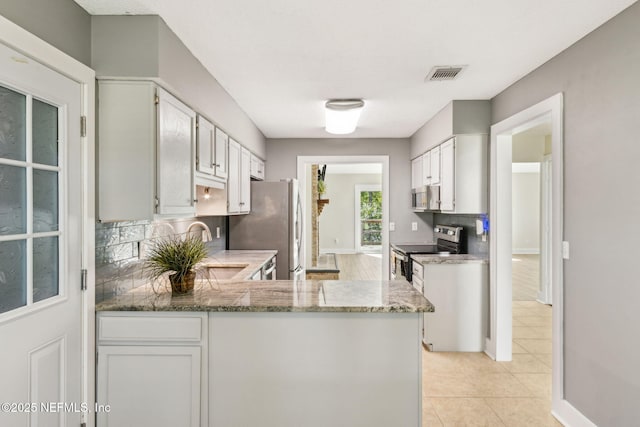 kitchen featuring visible vents, light stone counters, backsplash, stainless steel appliances, and a peninsula