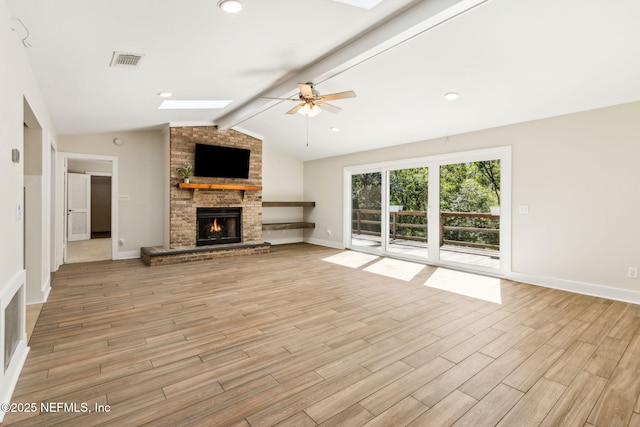 unfurnished living room with light wood-type flooring, visible vents, lofted ceiling with skylight, a brick fireplace, and ceiling fan