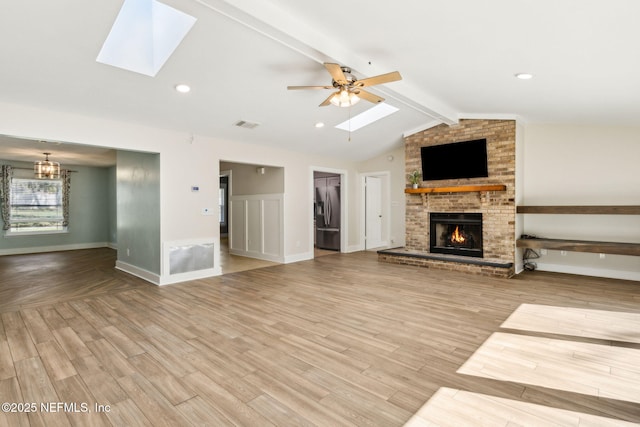 unfurnished living room featuring a brick fireplace, vaulted ceiling with skylight, wood finished floors, and ceiling fan