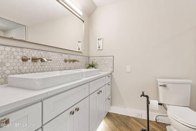 bathroom with toilet, backsplash, wood finished floors, baseboards, and vanity