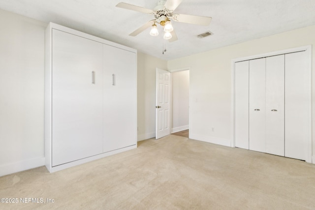 unfurnished bedroom with light carpet, visible vents, two closets, and baseboards