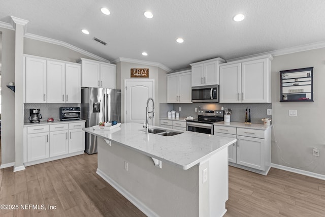 kitchen featuring visible vents, light wood-type flooring, a center island with sink, a sink, and appliances with stainless steel finishes