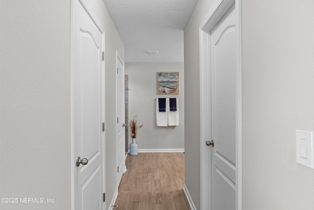 hall featuring baseboards, a textured ceiling, and light wood finished floors