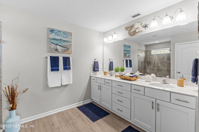 bathroom with visible vents, tiled shower, wood finished floors, and a sink