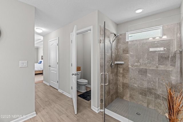 ensuite bathroom featuring wood finished floors, a stall shower, ensuite bathroom, a textured ceiling, and toilet