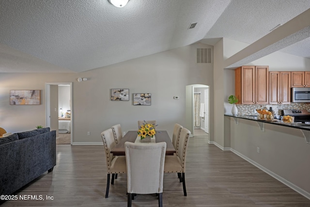 dining room with arched walkways, visible vents, lofted ceiling, and wood finished floors