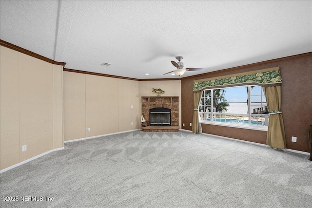 unfurnished living room featuring a ceiling fan, carpet floors, a fireplace with raised hearth, ornamental molding, and a textured ceiling