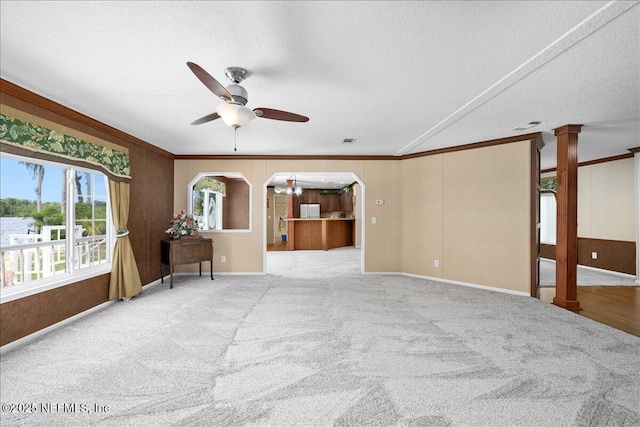 carpeted spare room with ornate columns, a textured ceiling, a ceiling fan, and ornamental molding