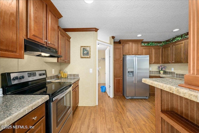 kitchen with stainless steel appliances, light countertops, under cabinet range hood, a textured ceiling, and light wood-type flooring