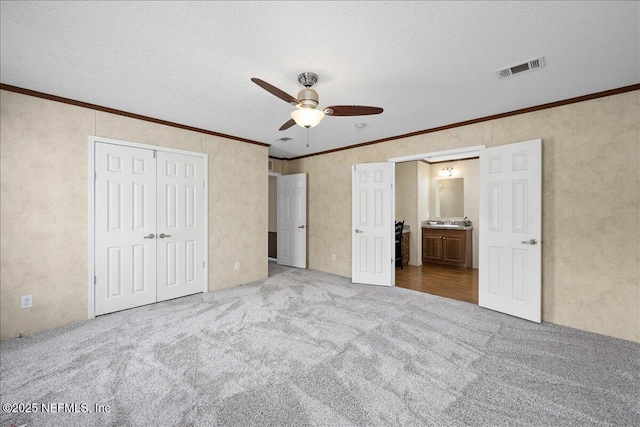 unfurnished bedroom featuring ornamental molding, a textured ceiling, a closet, carpet flooring, and ceiling fan